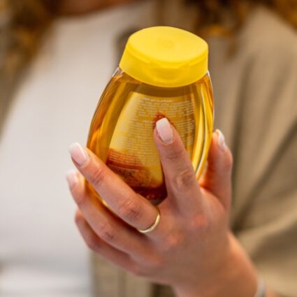 Smiling woman shopping for honey in a supermarket, holding a jar while carefully reading the label for nutritional information